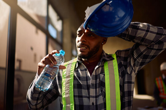 Exhausted black worker drinking water at construction site.