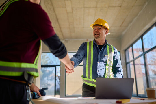 Happy mature foreman greeting worker at construction site.
