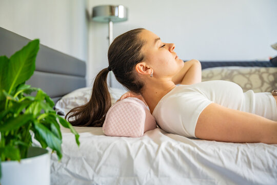 Woman positioning head on ergonomic orthopedic pillow for proper cervical spine support. Adjusting neck alignment before sleep to reduce pain, relieve tension and improve posture and sleep quality.