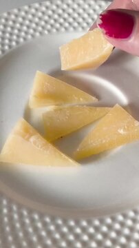 The hand takes a piece of cheese from the plate. Hard cheese in a woman's hand close-up. Calcium, potassium in products