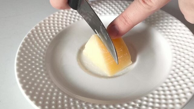 The hand uses a knife to cut the triangle of cheese in the plate. Hard cheeses. Calcium, potassium in lactic acid products
