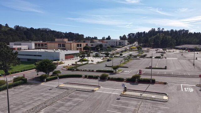 Wide aerial shot revealing the nearly deserted parking lot and campus of Skyline College in San Bruno, California, on a sunny day, showcasing the impact of remote learning or holidays
