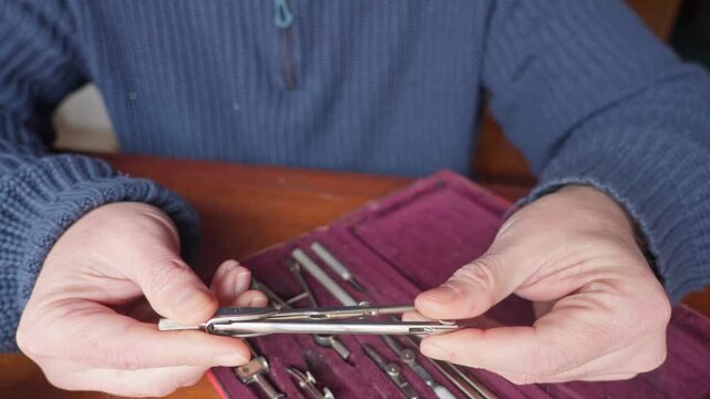 Medium shot of hands examining drafting tools in a fitted case, conveying careful inspection, quality control, and focused technical preparation.