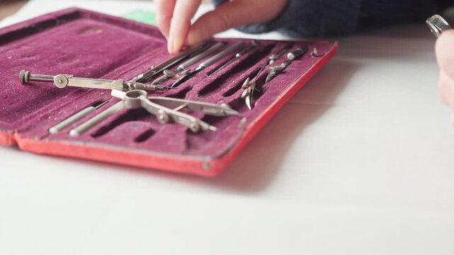Close-up of hands carefully placing drafting tools back into a fitted case, suggesting discipline, precision, and the end of a focused design session.