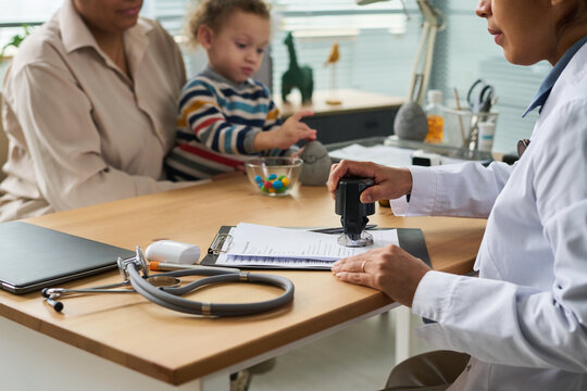 Mother holding toddler while female doctor stamping medical form during pediatric visit, showing child healthcare administration. Useful for insurance, clinic, parenting campaigns