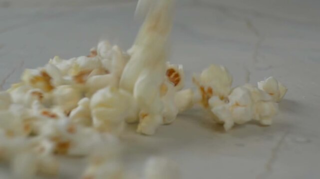 Fresh popcorn falling and bouncing into a pile on a textured marble surface in a close-up shot