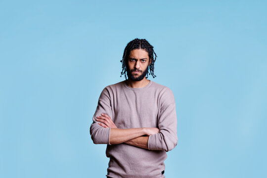 Arab angry man frowning eyebrows and standing with crossed arms portrait. Young arabian person looking at camera with folded hands and disapproval negative facial expression