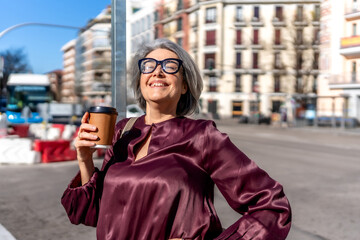 Obraz premium Mature woman enjoying sunrays with coffee on city street