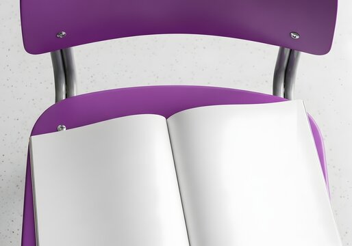 Top down view of an open blank white magazine or catalog mockup resting on the purple seat of a modern classroom or office chair, set against a light speckled floor background.