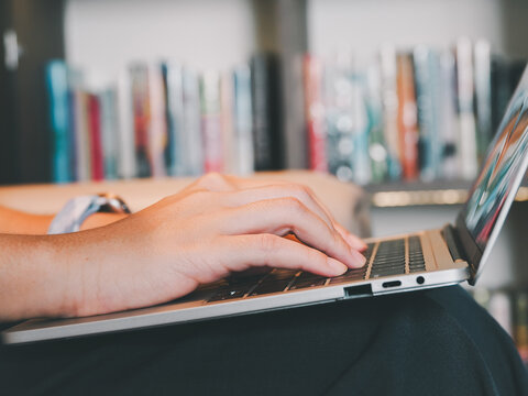 Hand typing laptop computer close up person office desk blurred bookshelf background work study copy space keyboard technology