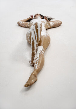 A woman lies on a white surface, her body covered in streaks of white paint. Her serene expression conveys a sense of calm and introspection