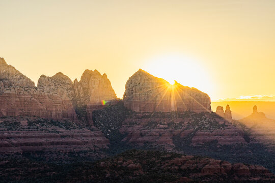 Starburst golden light behind jagged rock formation landscape