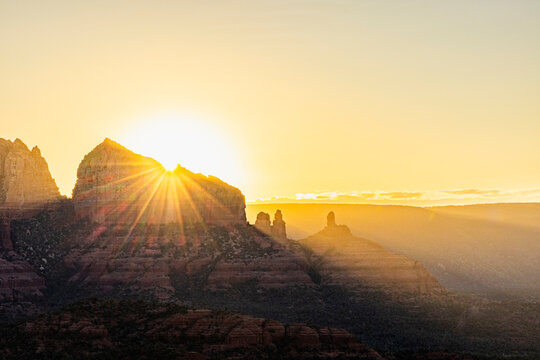 Starburst sunrise behind jagged rock formation landscape