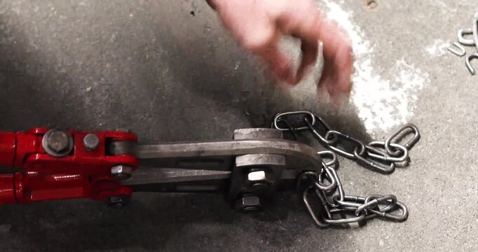 A man with large nippers cuts metal chain links of a given size.