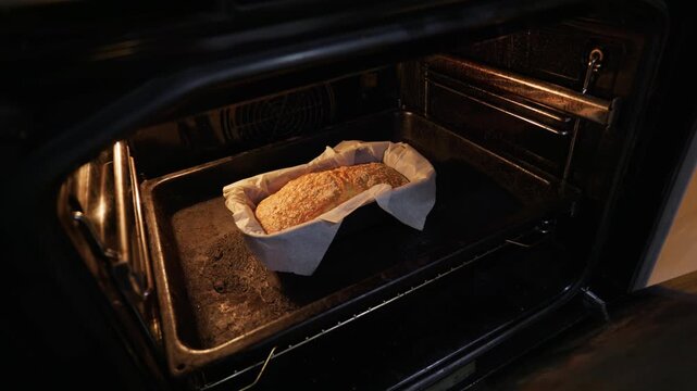 A fresh loaf of seeded bread bakes on parchment paper inside a warmly lit dark home oven. Concept of traditional domestic baking, comforting culinary lifestyle, and authentic food.