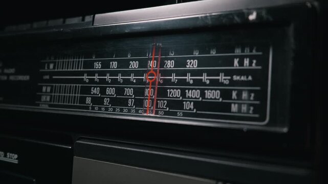 A red needle moves across the frequency dial of a vintage analog radio receiver. This detailed close-up shot highlights the retro design, various bands like UKW and MW, and signs of use.