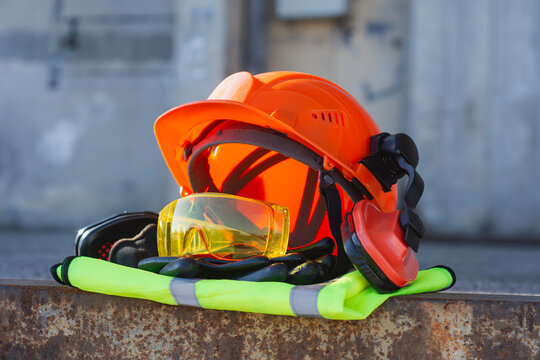 Professional safety gear with helmet with hearing protection eye shields and reflective vest on a rusty metal surface. Concept of workplace security labor protection in construction or heavy industry.