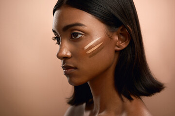 Fototapeta premium Cosmetic, lines and woman with foundation in studio, contour swatch and shade test for natural beauty. Makeup, space and person with highlighter for glow aesthetic, skin tone and brown background