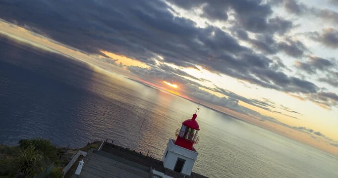Hyperlapse of Ponta do Pargo lighthouse on dramatic cliffs during sunset over the Atlantic Ocean in Madeira, Portugal. Aerial backward