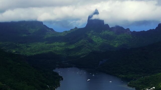 dramatic Mount Rotui above Opunohu Bay in Moorea, French Polynesia, aerial drone view of with sailboats resting on the bay below steep green slopes and low clouds circle right motion