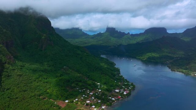 Mount Rotui and Opunohu Bay in Moorea, French Polynesia, aerial drone view of with tropical lush green ridges descending toward calm bay water beneath a low cloud ceiling forward pan up motion