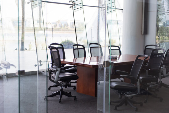 Empty glass walled conference room with wooden table and ergonomic swivel chairs overlooking waterfront