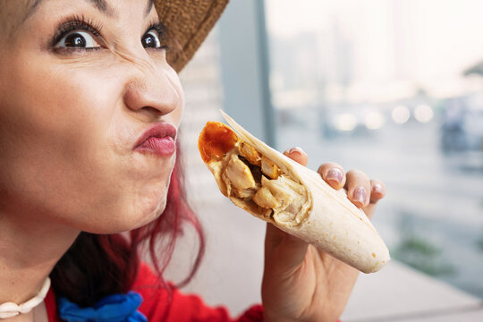 Woman making a suspicious, disgusted face while smelling a chicken wrap or burrito with sauce, reacting to an unpleasant odor and questioning food freshness