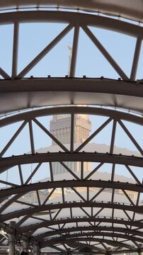 A stunning view of the Makkah Royal Clock Tower rising majestically between modern high-rise buildings in Mecca, Saudi Arabia. The iconic clock face stands tall against the sky, symbolizing Islamic he