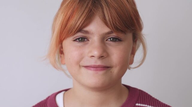 Closeup portrait face of happy caucasian girl elementary school blond ginger redhead hair, smiling, grey eyes. Looking at camera. Positive mood, joyful, cheerful kid child, laugh over white background