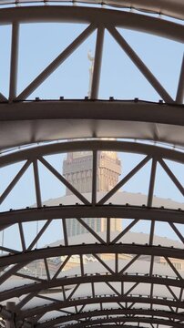 A stunning view of the Makkah Royal Clock Tower rising majestically between modern high-rise buildings in Mecca, Saudi Arabia. The iconic clock face stands tall against the sky, symbolizing Islamic he