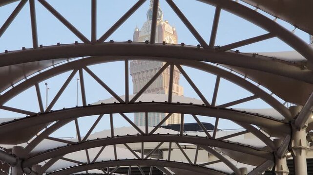 A stunning view of the Makkah Royal Clock Tower rising majestically between modern high-rise buildings in Mecca, Saudi Arabia. The iconic clock face stands tall against the sky, symbolizing Islamic he