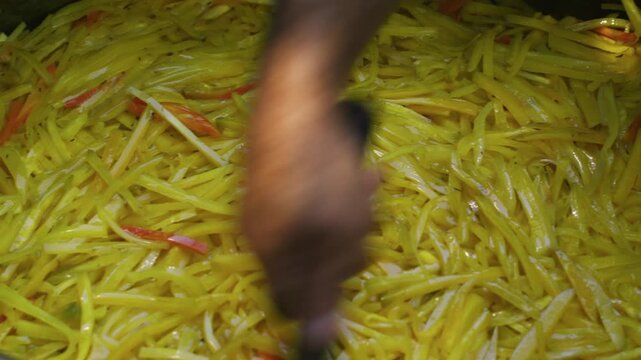 Chef Smoothing Sliced Carrots in Large Metal Cauldron for Plov, Close Up