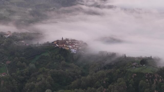 Aerial view of the historic town of Reggello emerging from thick morning fog and mist surrounded by lush green hills and forests Reggello, Tuscany, Italy.