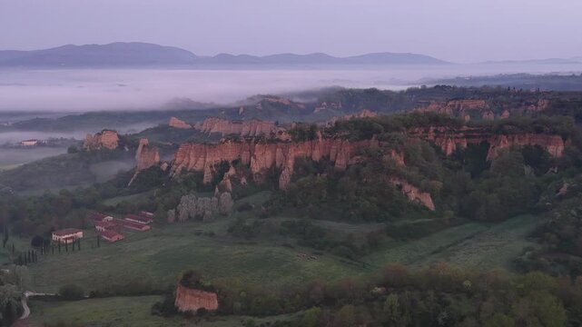 Aerial view of the unique Balze clay formations rising above the morning mist and green hills in Reggello, Tuscany, Italy.