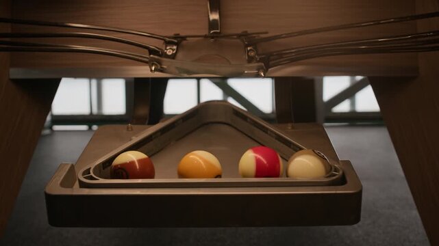 Close up shot of billiard balls rolling through internal table return system toward triangle rack, with automatic collection mechanism in pool table