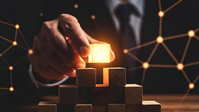 Business foundation and infrastructure development. Networking and partnership connections. Businessman building a pyramid of wooden blocks with a glowing top piece and digital node overlay
