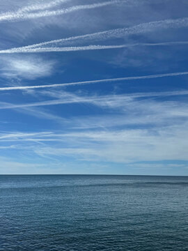 Calm sea and blue sky with clouds and contrails vertical.