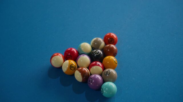 Close up shot of colorful billiard balls tightly grouped on blue pool table surface, ready for break shot