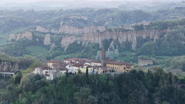 Aerial view of a historic village with a church tower and the unique Balze del Valdarno clay cliffs in Reggello, Tuscany, Italy.