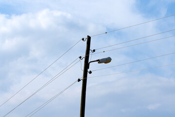 Fototapeta premium A utility pole featuring electrical power lines and a mounted street light against a blue sky, serves as urban infrastructure for both power distribution and public lighting. 