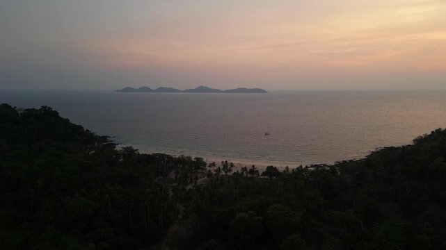 Koh Mook, Thailand: Cinematic aerial drone footage of the sunset over Koh Muk with the Kradan island in the background in Thailand. Shot with a forward motion above palm tree lining Charlie beach