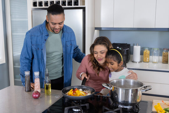 Family parents and daughter cooking peppers and mushrooms in frying pan on kitchen island stove
