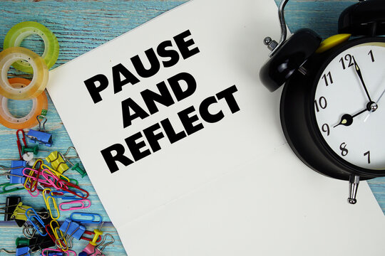 Pause and Reflect text with alarm clock and colorful office supplies on a blue wooden surface