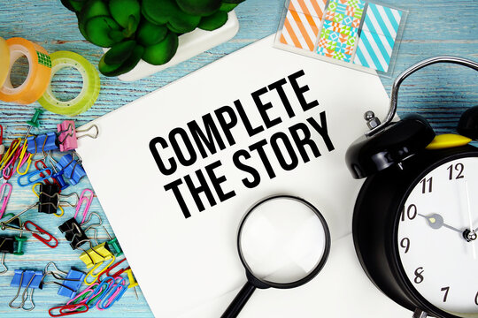 Complete The Story text on a paper surrounded by office supplies, a magnifying glass, and a clock on a blue wooden surface