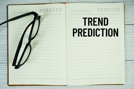 Notepad with message "Trend Prediction" and eyeglass on wooden background