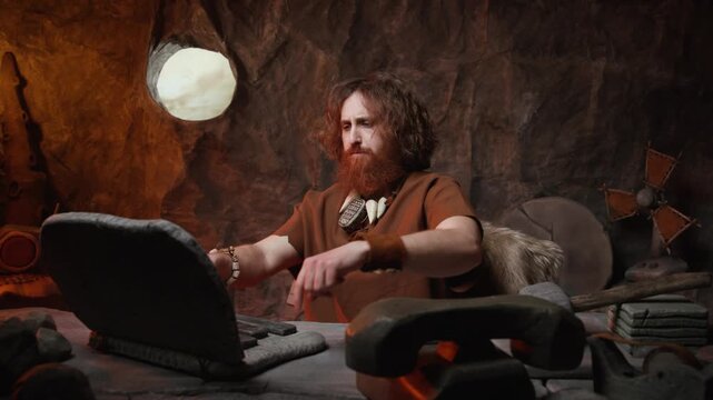 Enthusiastic caveman businessman making a phone call on a stone handset while working on his laptop