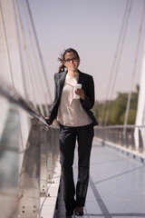 Fototapeta premium Business woman walking on bridge with coffee cup, smiling in professional attire during commute
