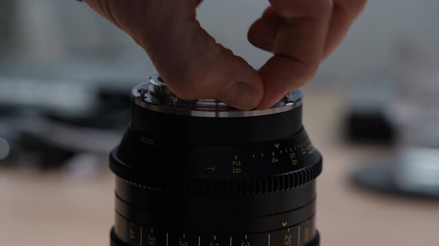 Side angle view of hands unscrewing and removing an EF bayonet mount from a cinema lens. Smooth disassembly process clearly visible. First step of an EF to PL mount conversion.