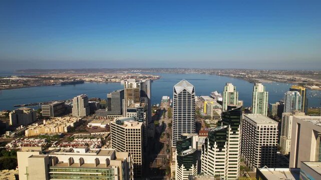 Drone flying backward above downtown San Diego at 9AM facing the harbor with camera slowly tilting down to reveal streets below.