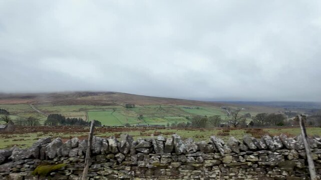 North Pennines rural landscape with green fields, rolling hills, and dry stone wall under cloudy sky